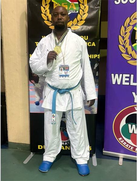 A man in a white karate outfit standing next to a banner.