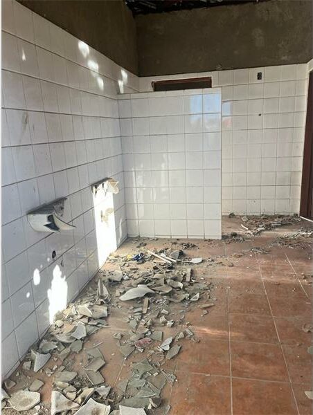 A bathroom with broken tiles and broken walls.