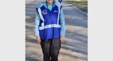 A woman in a blue jacket and black pants is standing on a paved path.