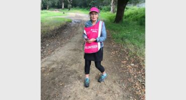 A woman in pink hat and pink shirt standing on a dirt road.