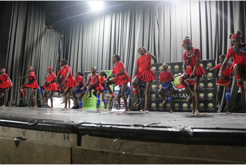 A group of children in red dresses performing on stage.