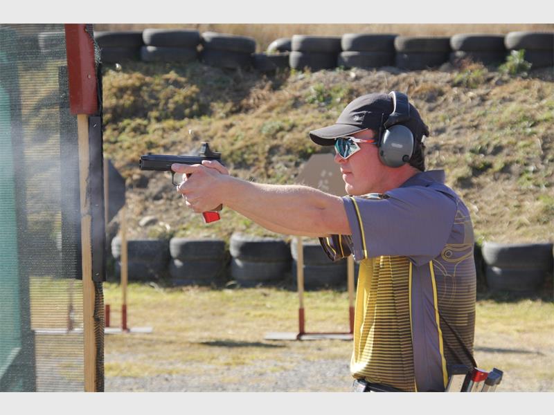 A man in a yellow shirt and black hat aiming a gun.