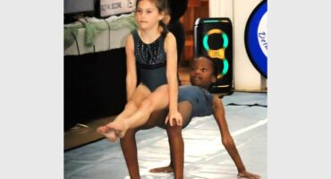 Two young girls are doing gymnastics on a mat.