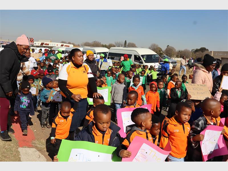 Children walking in a line with adults holding signs.