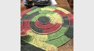 A knitted rug on a table with a green, red and yellow design.