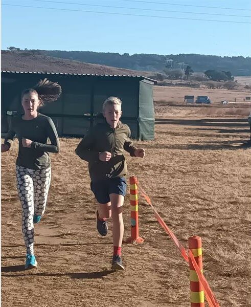Two people running in a race on a dirt field.