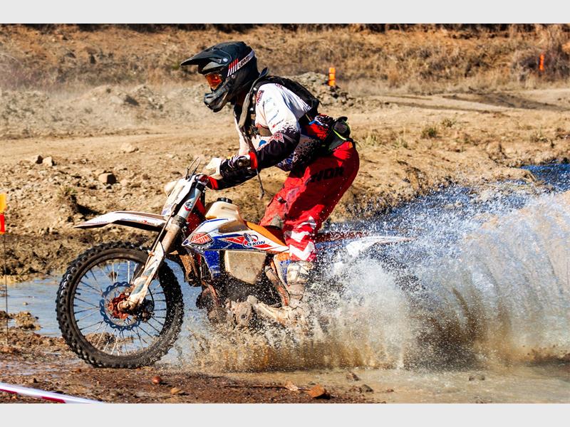 A man riding a dirt bike through a muddy area.