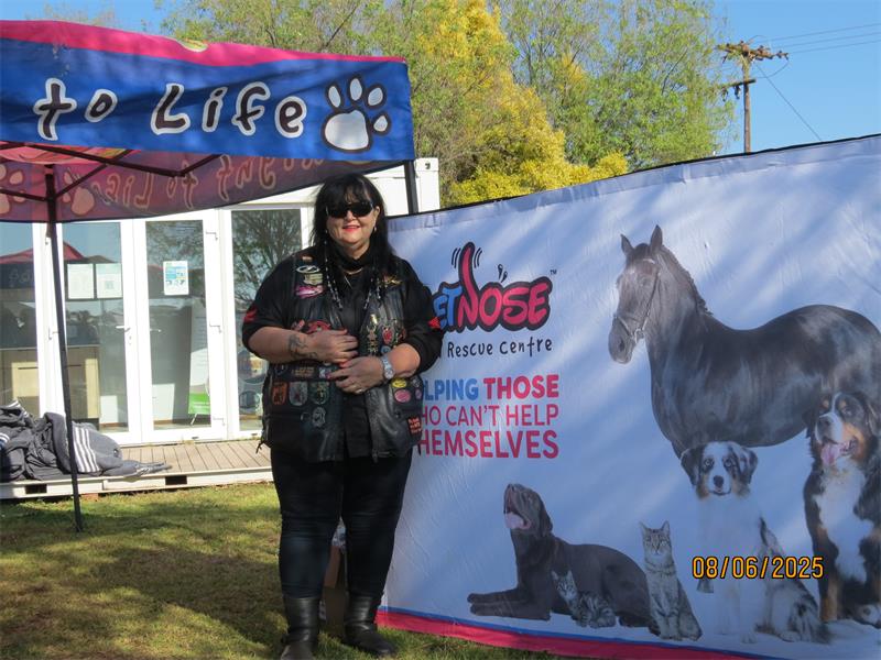 A woman standing in front of a banner with a dog and a horse.