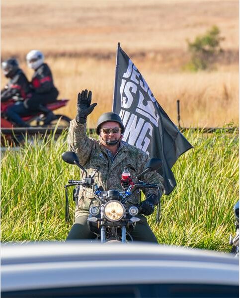 A man waving a black flag on a motorcycle.