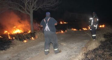 Two men standing on a dirt road near a fire.