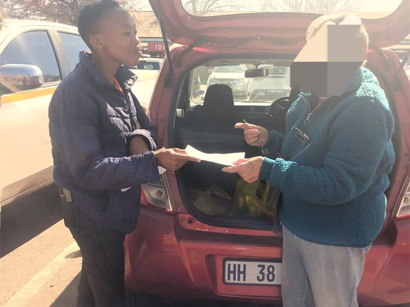 A man handing a piece of paper to another person in a car.