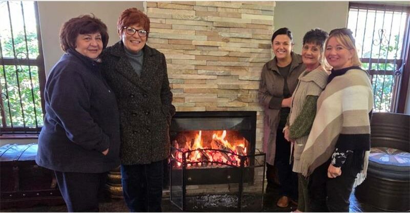 Four women standing next to a fireplace with a fire.