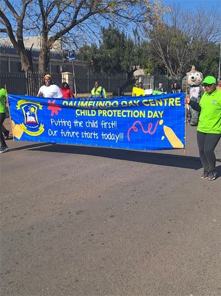People in green shirts and yellow shirts holding a banner.
