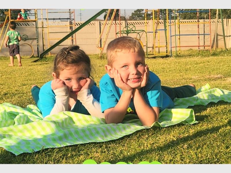 Two children laying on a blanket in the grass.