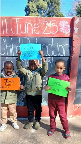 Three children holding up signs in front of a chalkboard.