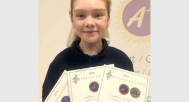 A girl holding three certificates in front of a wall.