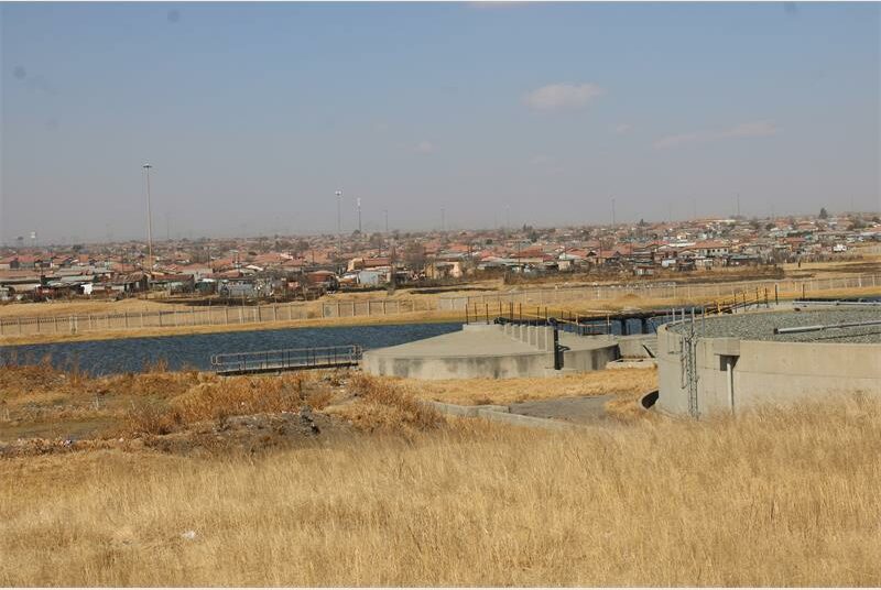 A view of a large field with a water treatment plant in the background.