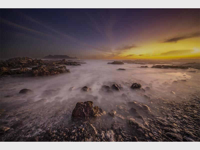 A sunset over the ocean with rocks and water.