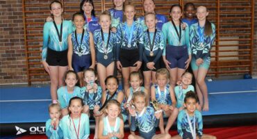 A group of girls posing for a photo on a gymnastics mat.