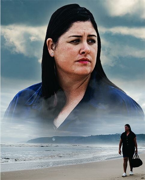 A woman is walking on the beach with a bag.