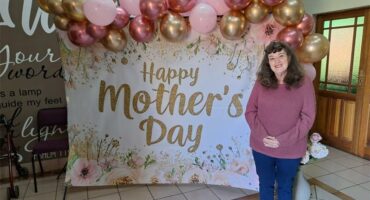 A woman standing in front of a happy mother's day banner.