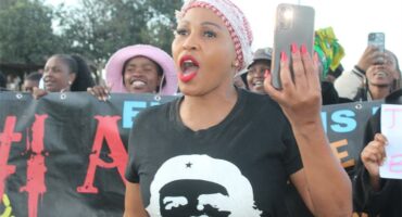 A woman holding a cell phone while standing in front of a crowd.