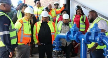 A group of people in hard hats and safety vests standing around a blue water pipe.