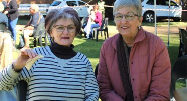 Two older women sitting at a table in the grass.