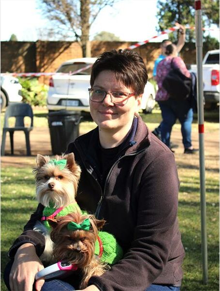 A woman in a green sweater holding two small dogs.