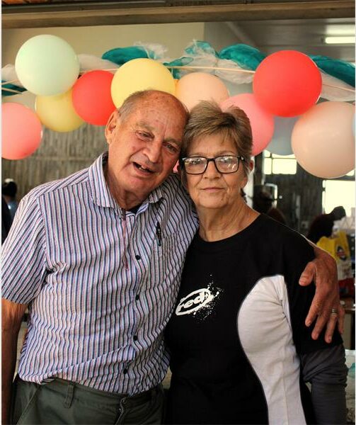 An older couple posing for a photo in front of balloons.