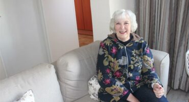 An older woman sitting on a couch in a living room.