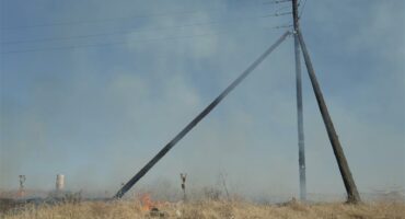 A fire burns near a power pole in a field.