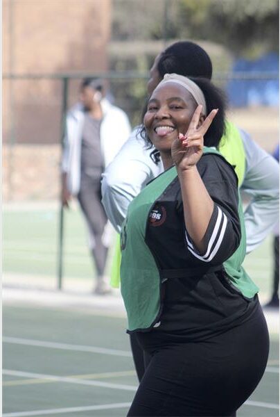 A woman in a green shirt and black pants is giving the peace sign.