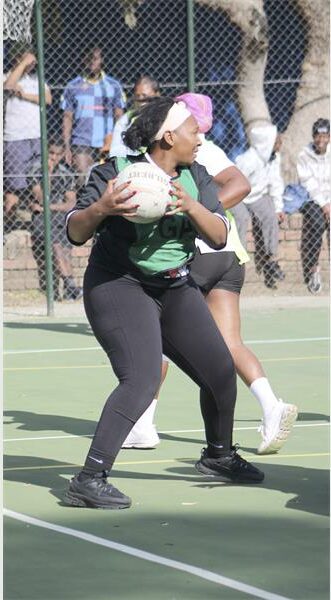 A woman in a green shirt and black pants is holding a ball.