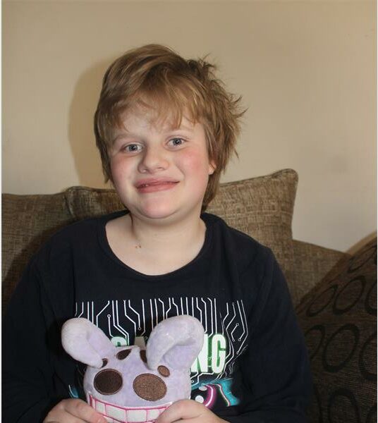 A boy sitting on a couch holding a stuffed animal.