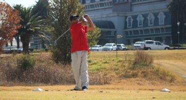 A man in red shirt playing golf in front of a building.