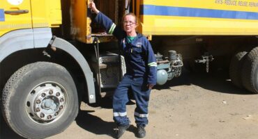 A woman standing next to a large yellow truck.