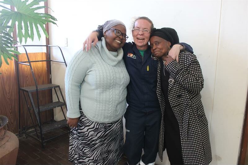 Three people standing together in a room with a man hugging one of the women.