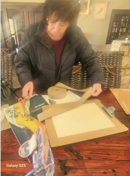 A woman cutting paper on a table with a knife.