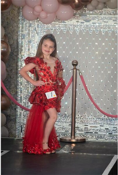 A young girl in a red dress standing on a stage.