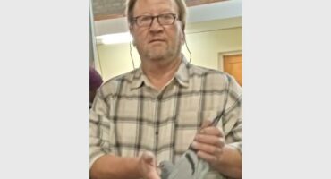 A man with glasses and a plaid shirt holding a small dove.