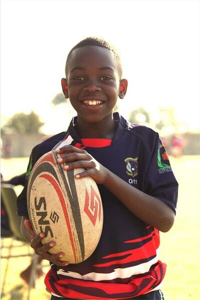 A young boy holding a rugby ball in a field.
