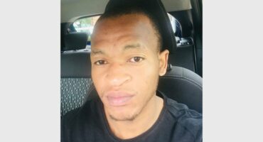 A man in a black shirt sitting in the back seat of a car.