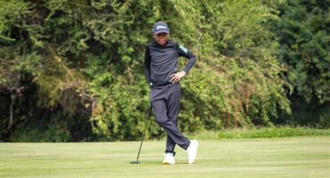 A man in black shirt and black pants is standing on a golf course.