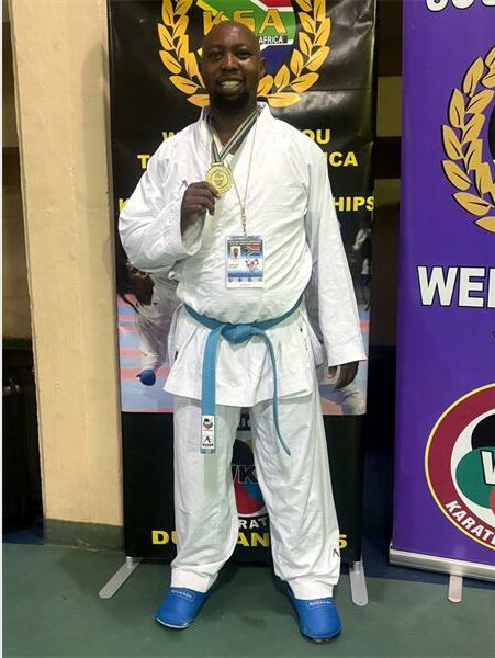 A man in a white karate outfit standing next to a banner.