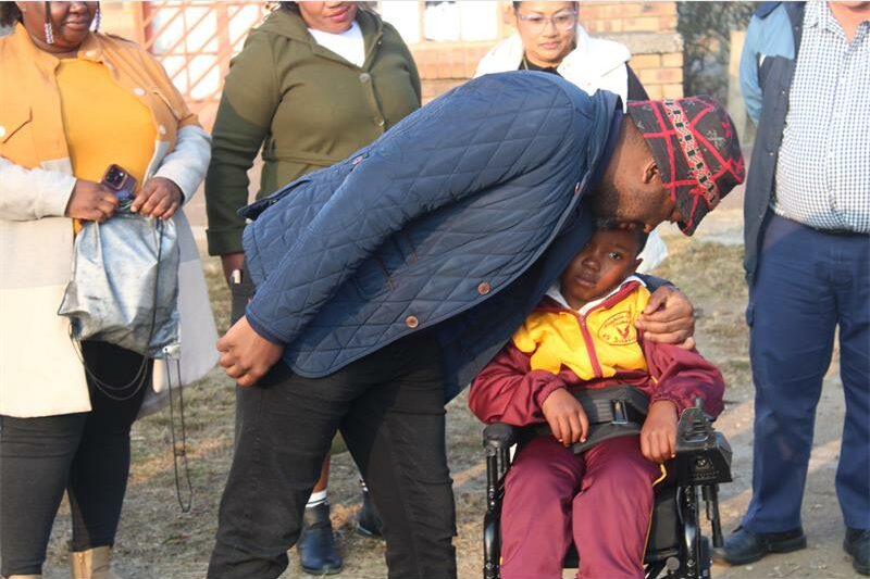 A man in a wheelchair is being hugged by a child.