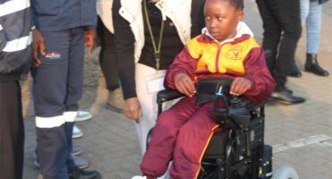 A young child in a wheelchair with a woman standing next to her.