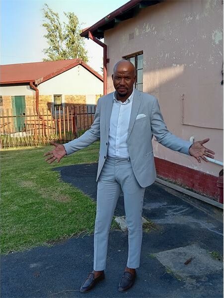 A man in a suit and tie standing in front of a house.
