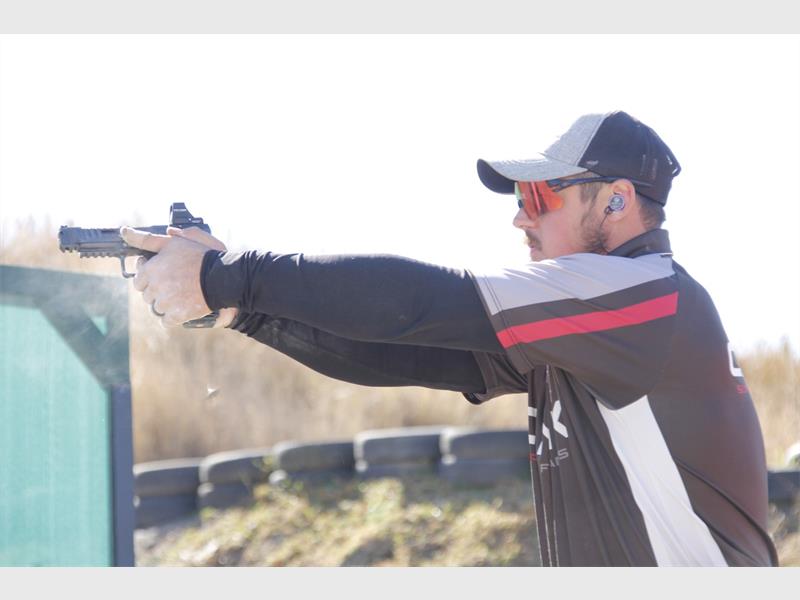 A man in sunglasses aiming a gun at a target.
