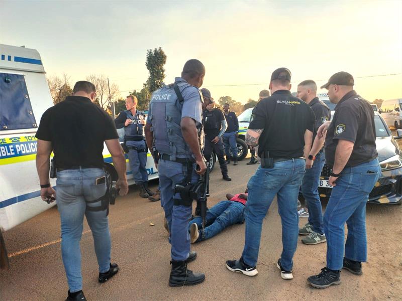 Police officers stand around a man lying on the ground.